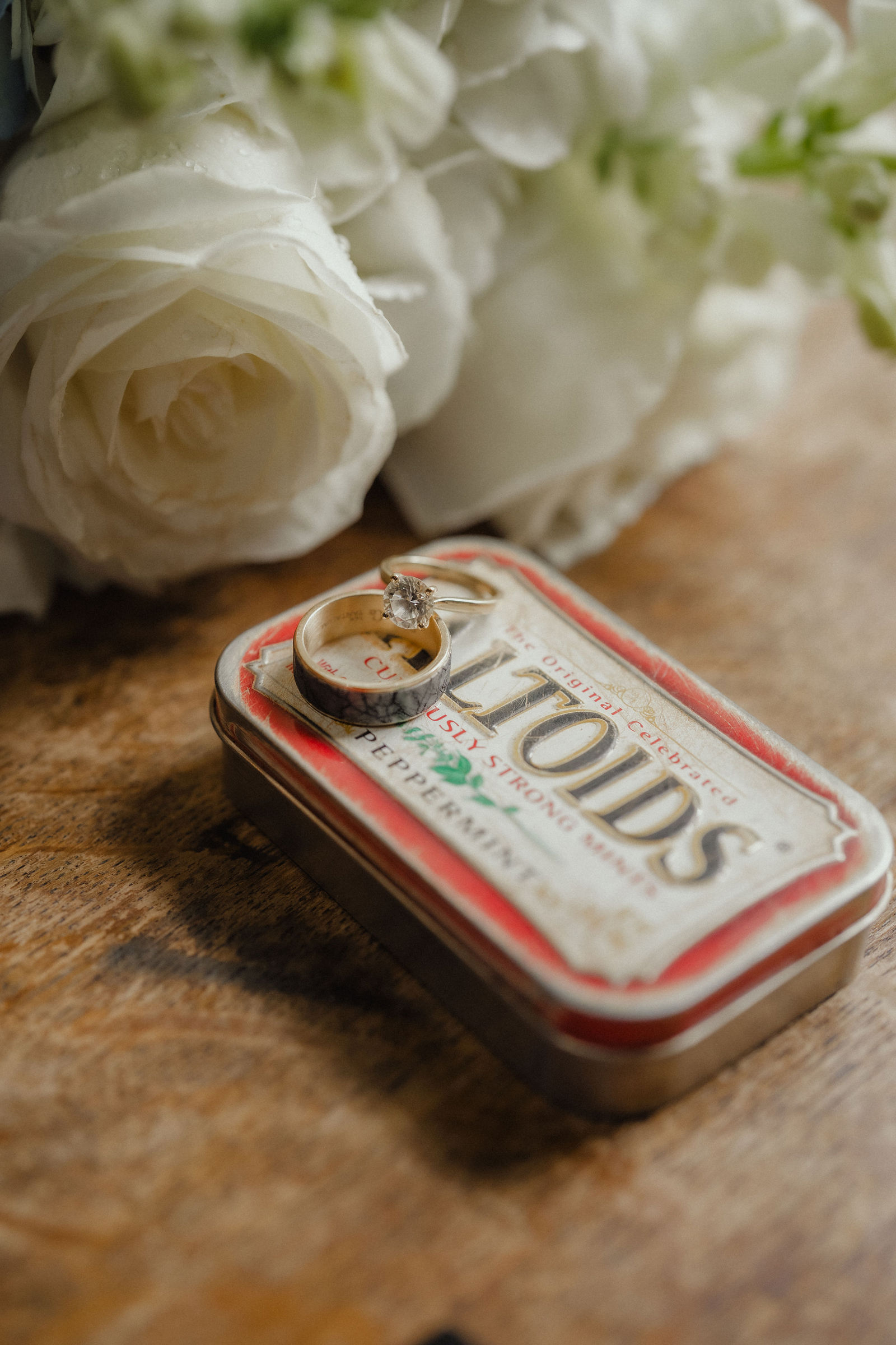 Their wedding rings in an Altoids tin beside white roses