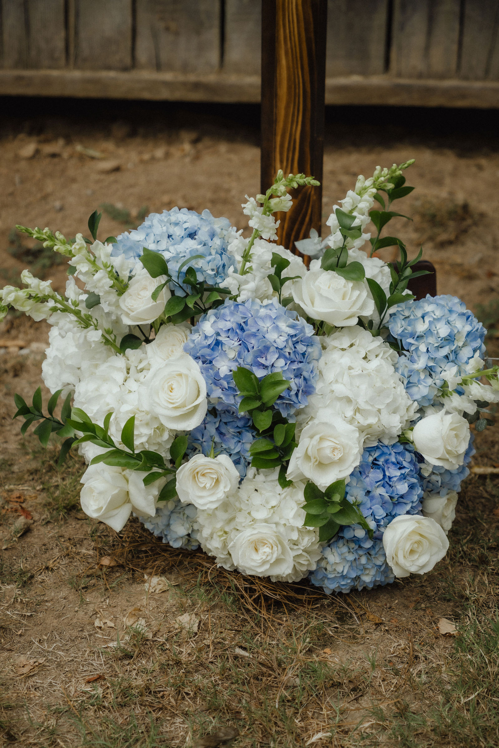 Blue hydrangea and white rose bouquet on the grass at the foot of the draped wooden cross