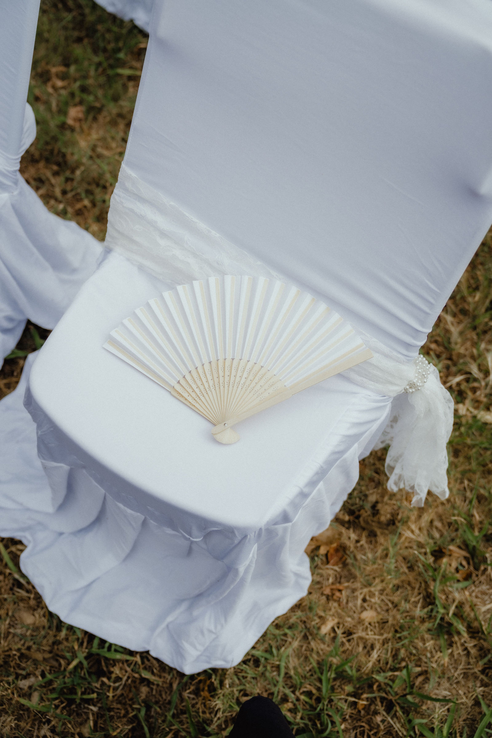A paper fan waiting on a white ceremony chair in the September heat