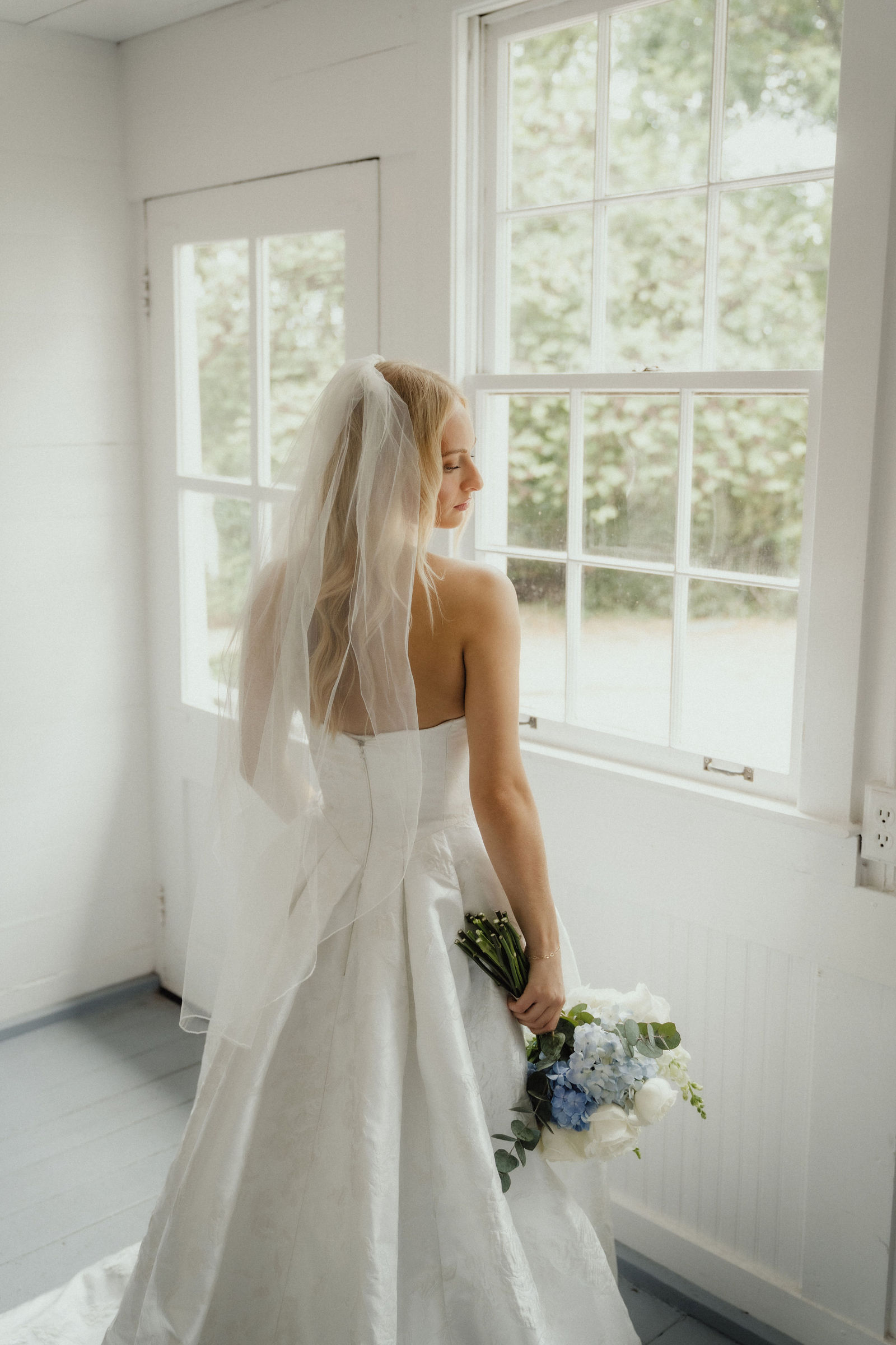 Denalyn at the window of the all-white getting-ready room, her train across the floor