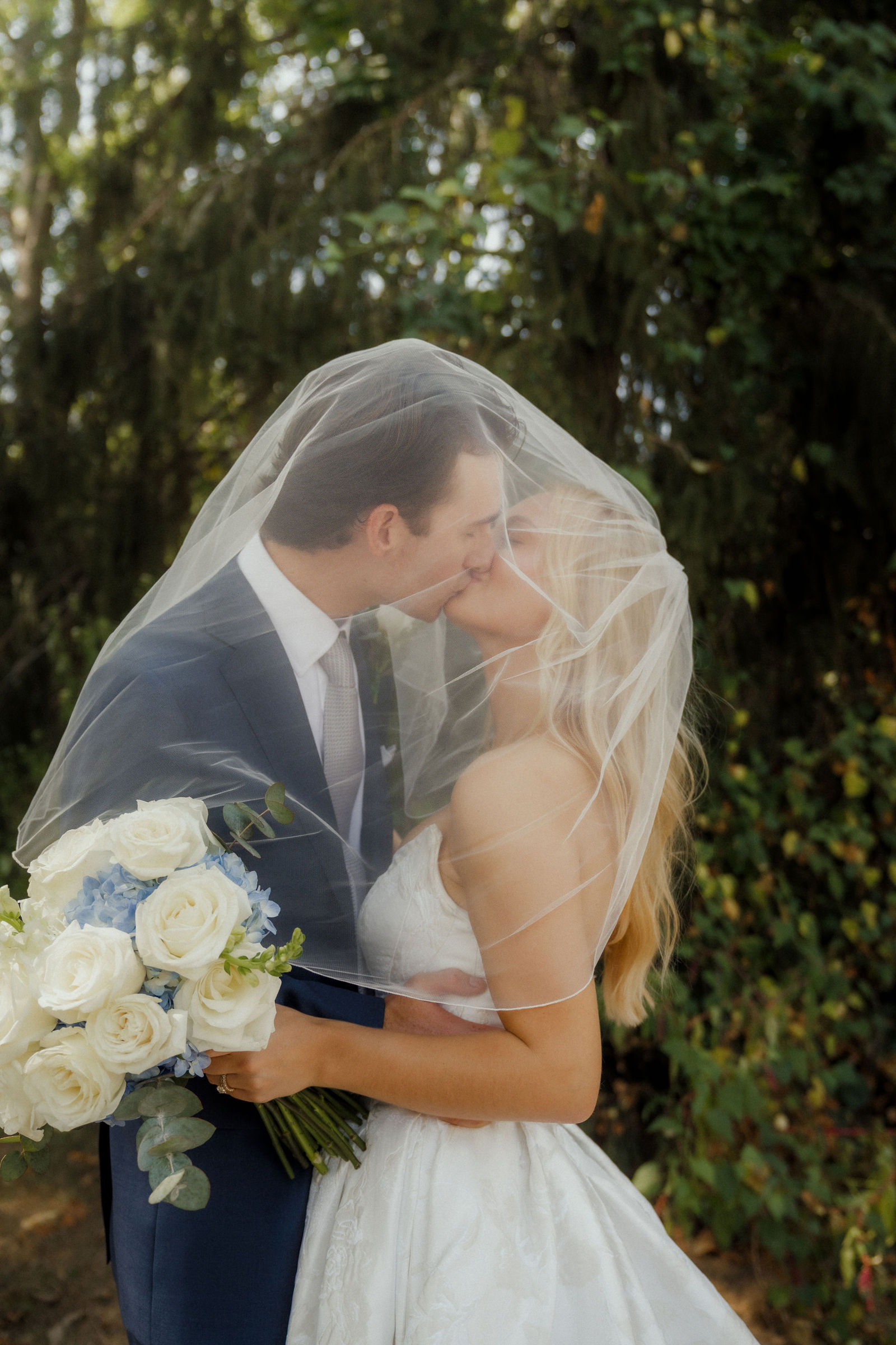 Denalyn and John kissing underneath her veil in the trees