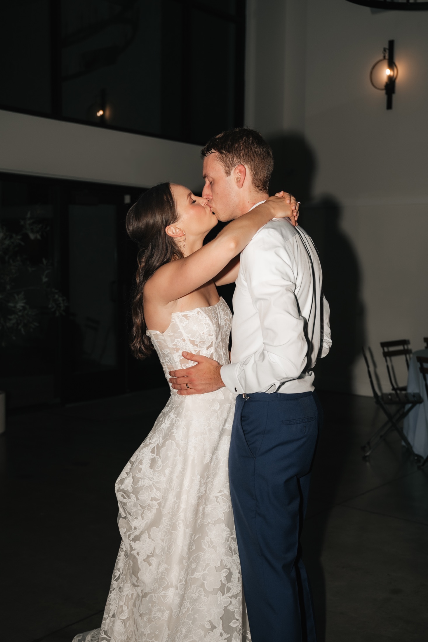 Katie and Zach kissing beneath the reception lights