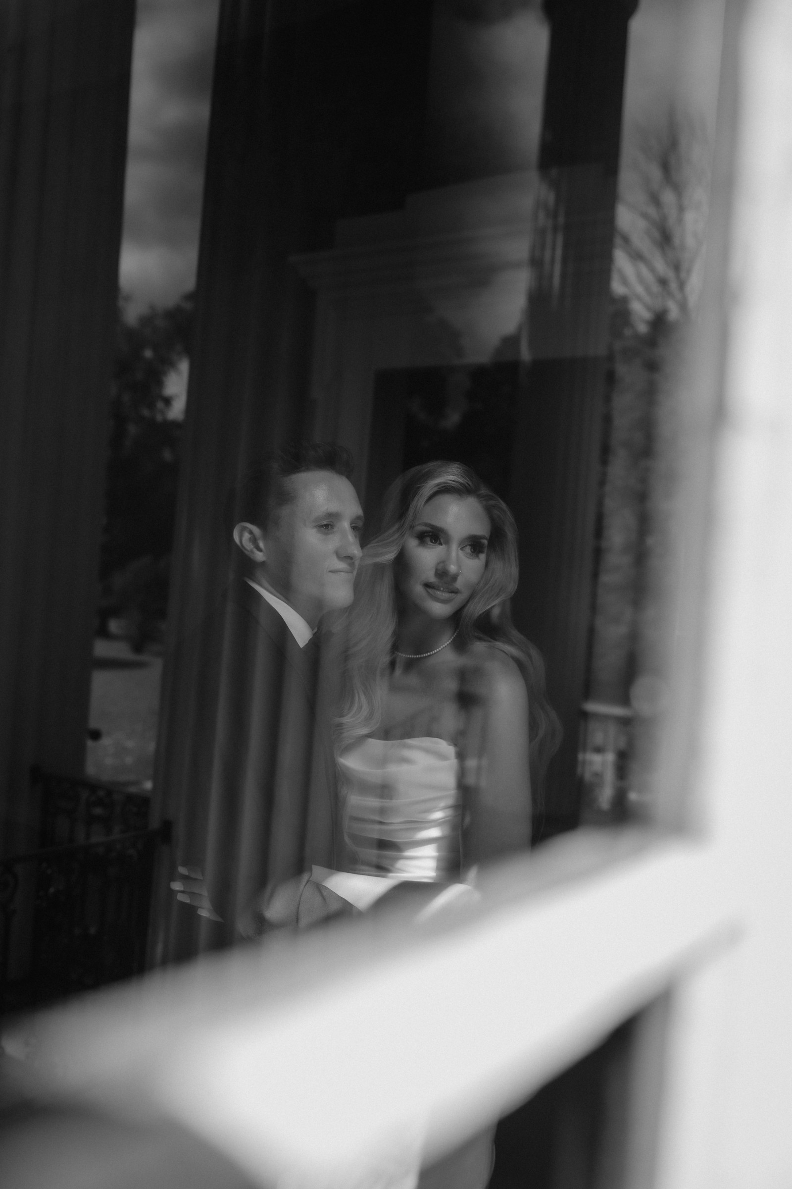 Maddie and Brandon reflected in the porch glass, columns and sky behind them