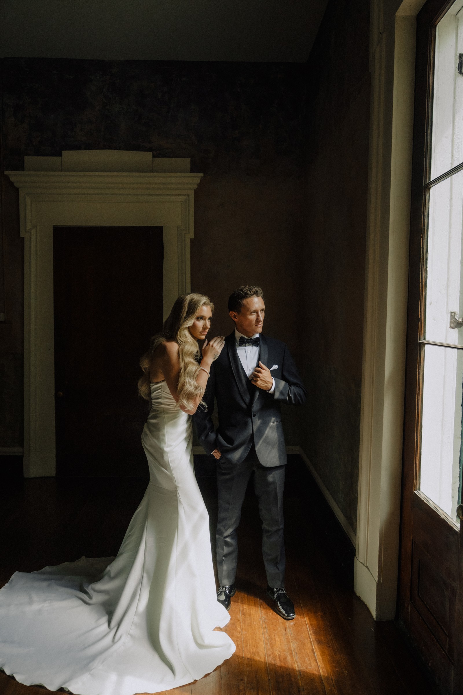Maddie and Brandon by the window against the dark plaster wall