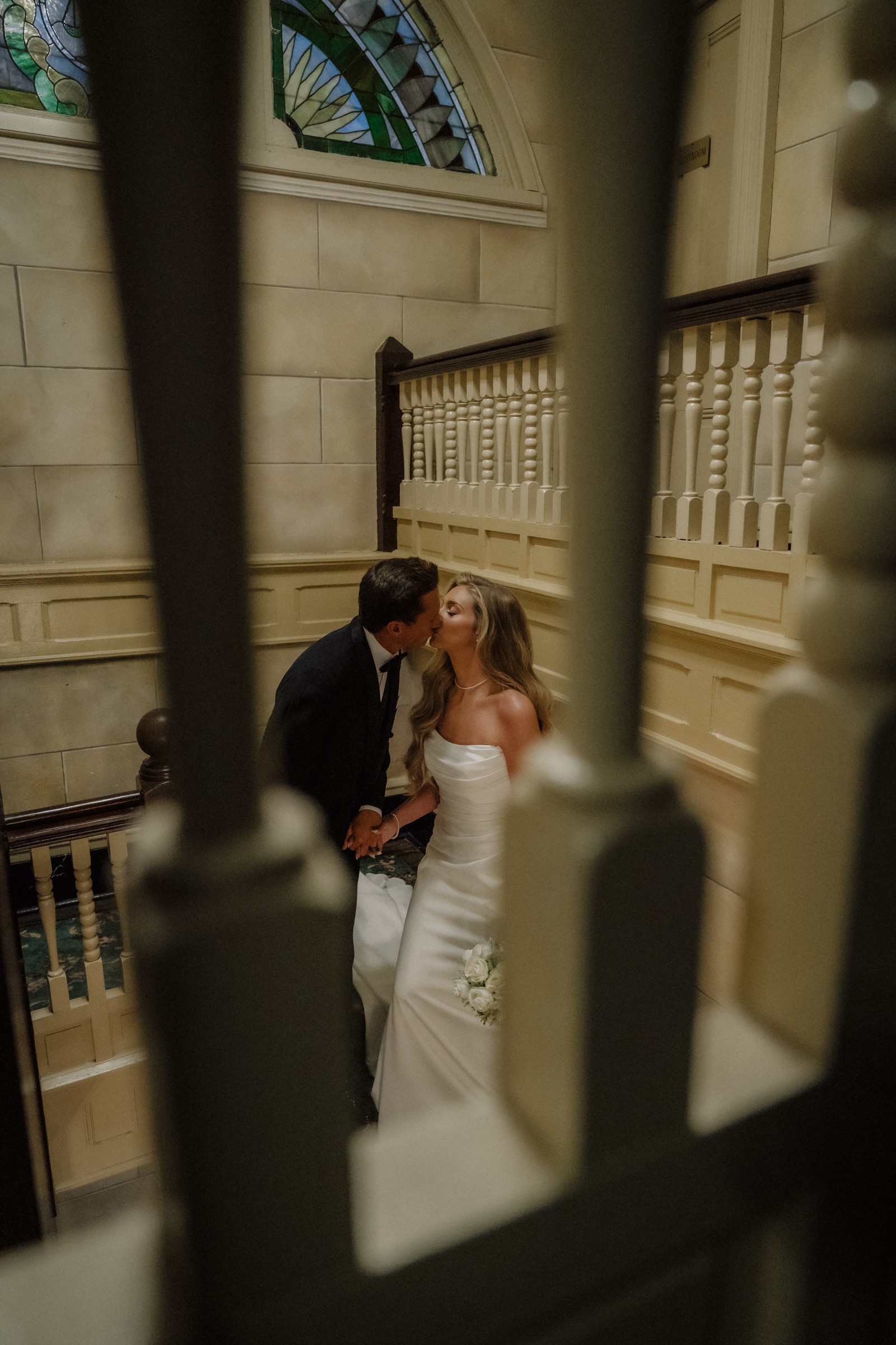 A kiss glimpsed through the balusters, stained glass above