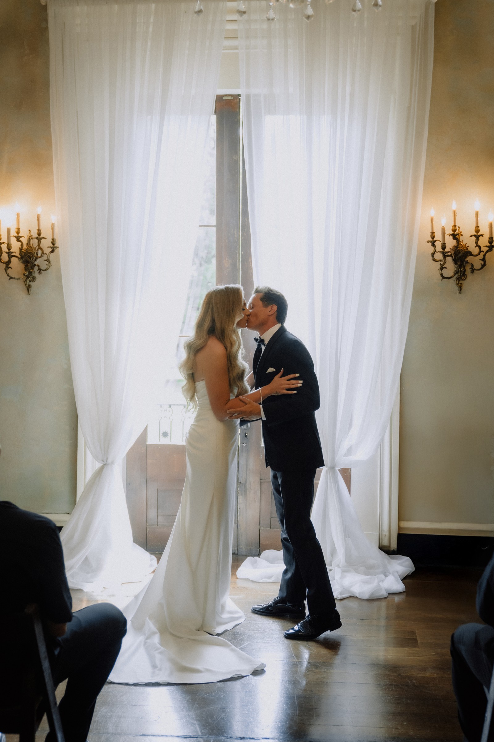 The kiss at the altar between sheer drapes and candle sconces