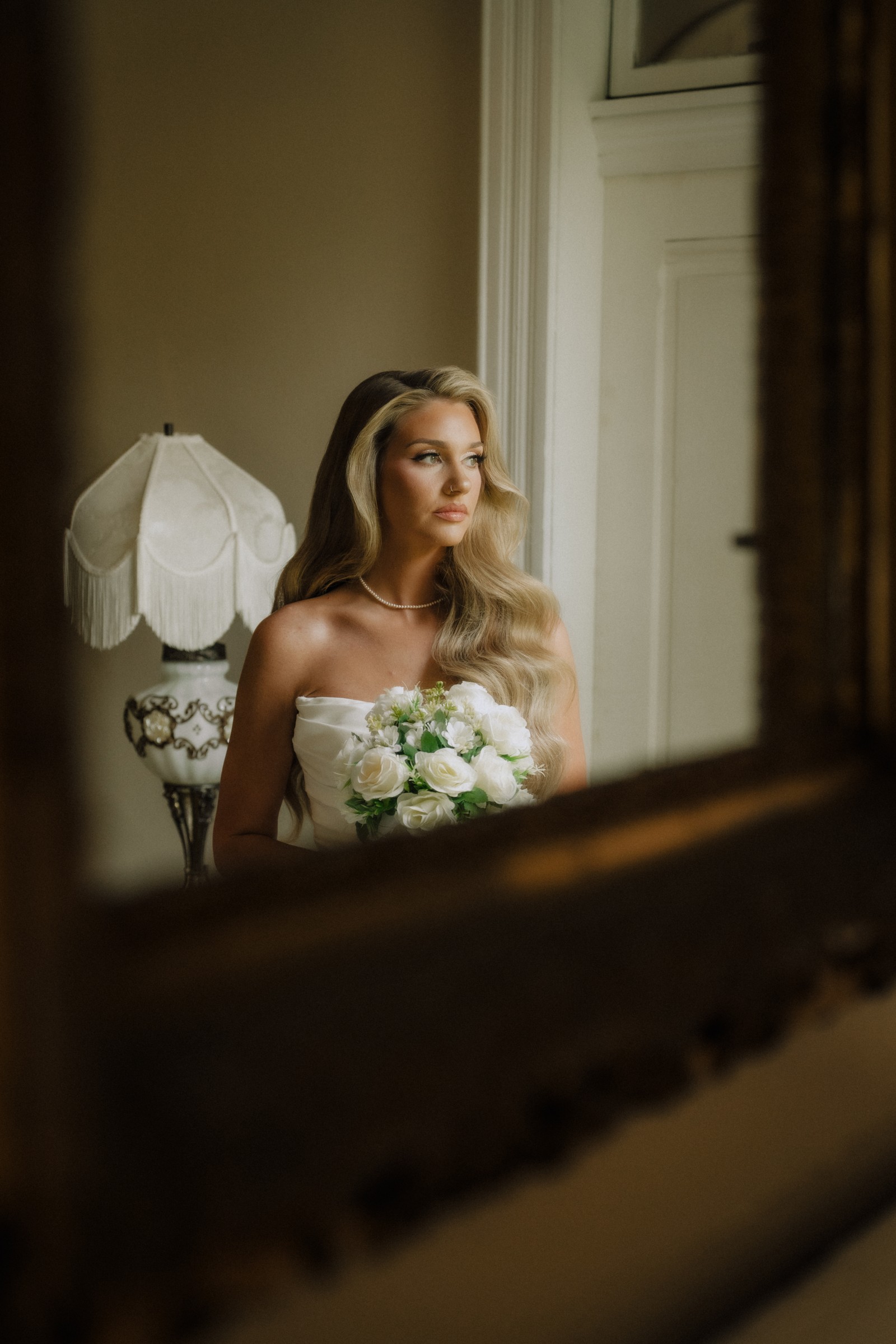 Maddie in the mirror with her bouquet, beside the fringed lamp