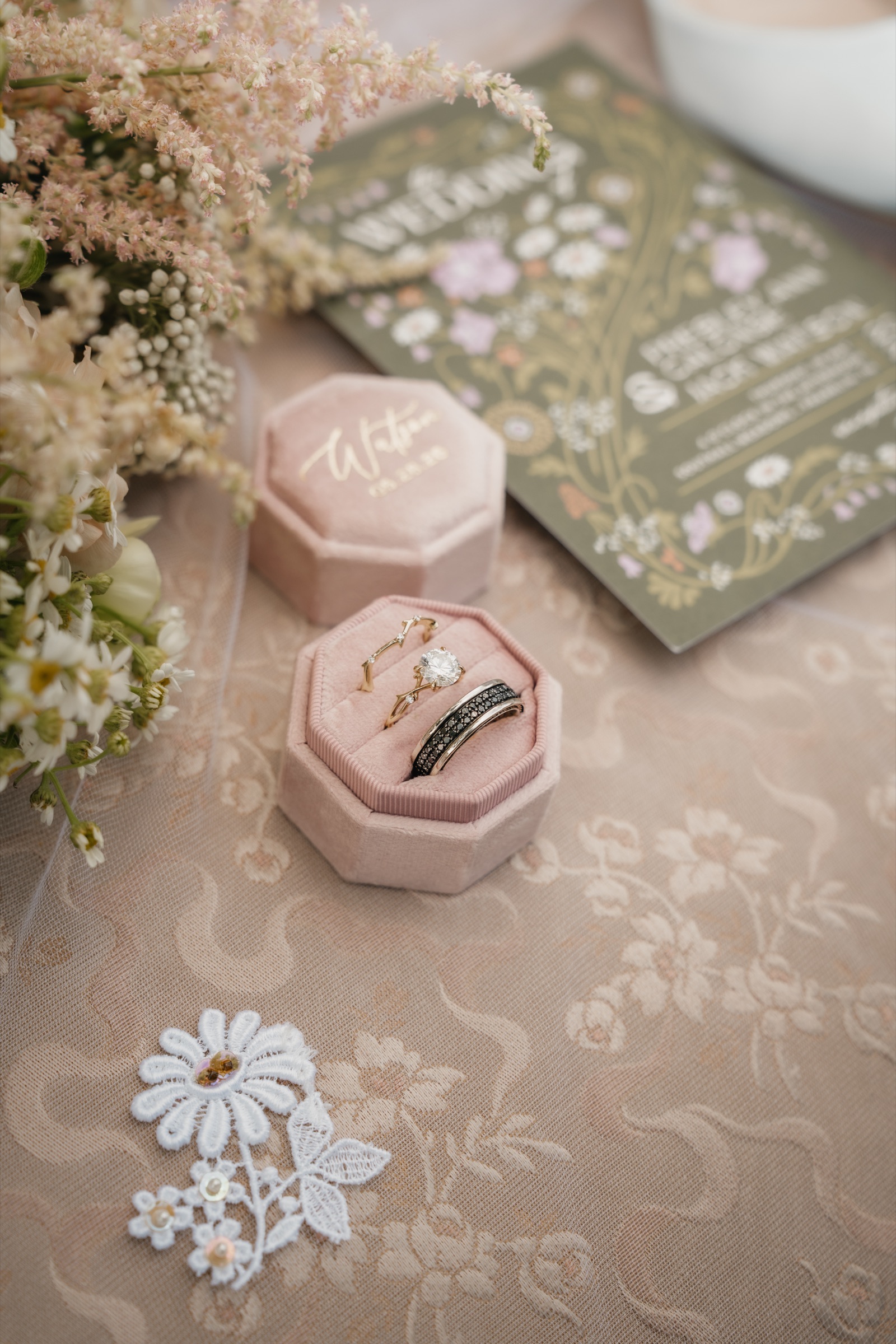 Presley and Jack’s rings in a pink velvet box beside their floral invitation suite