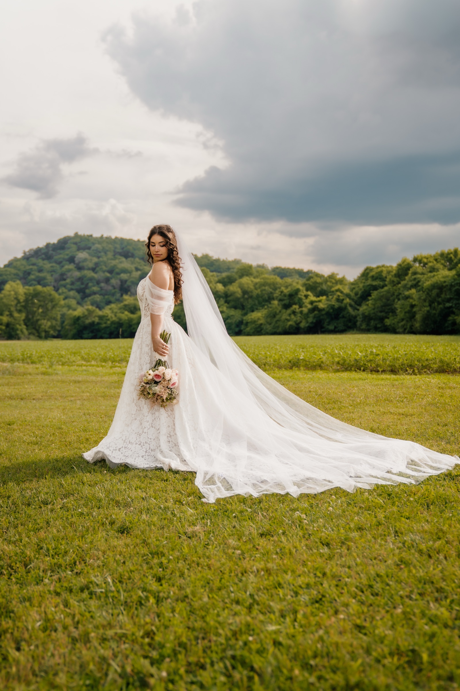 Presley standing in the open field, her veil and train sweeping the grass