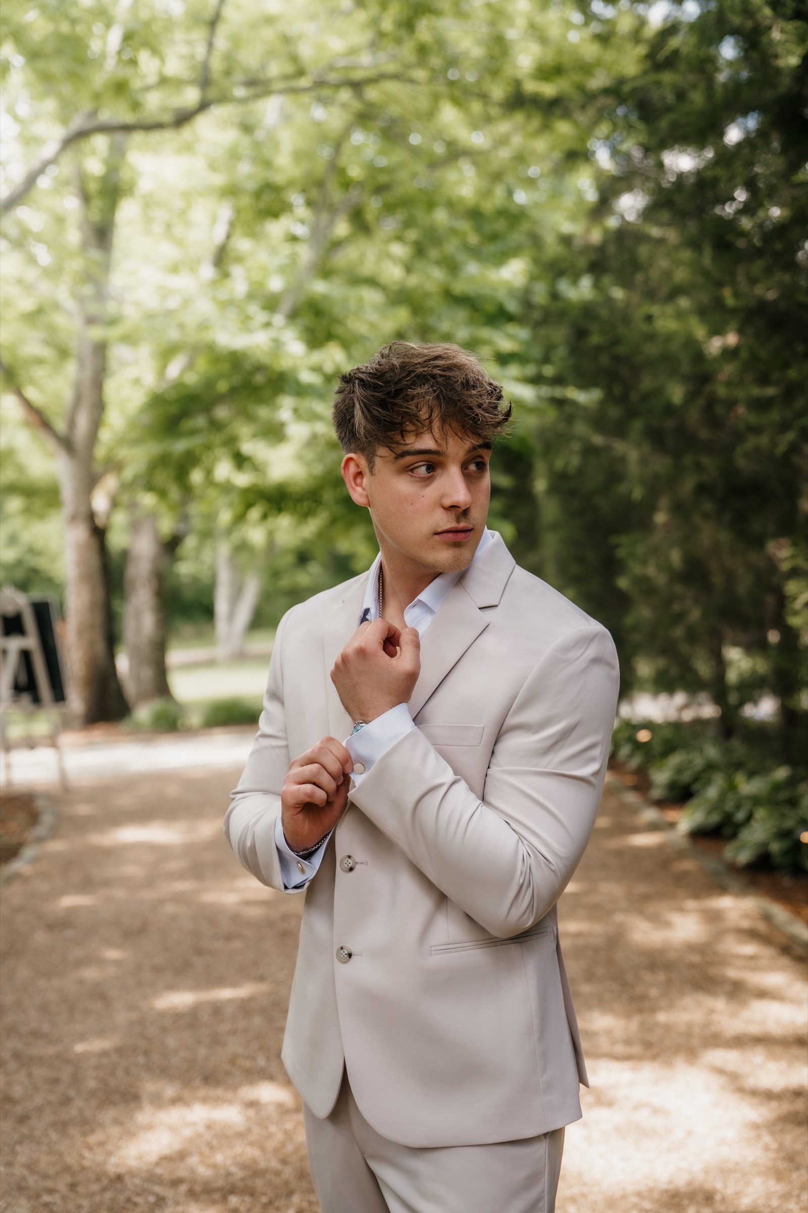 Jack fixing his cuff in his cream suit beneath the trees