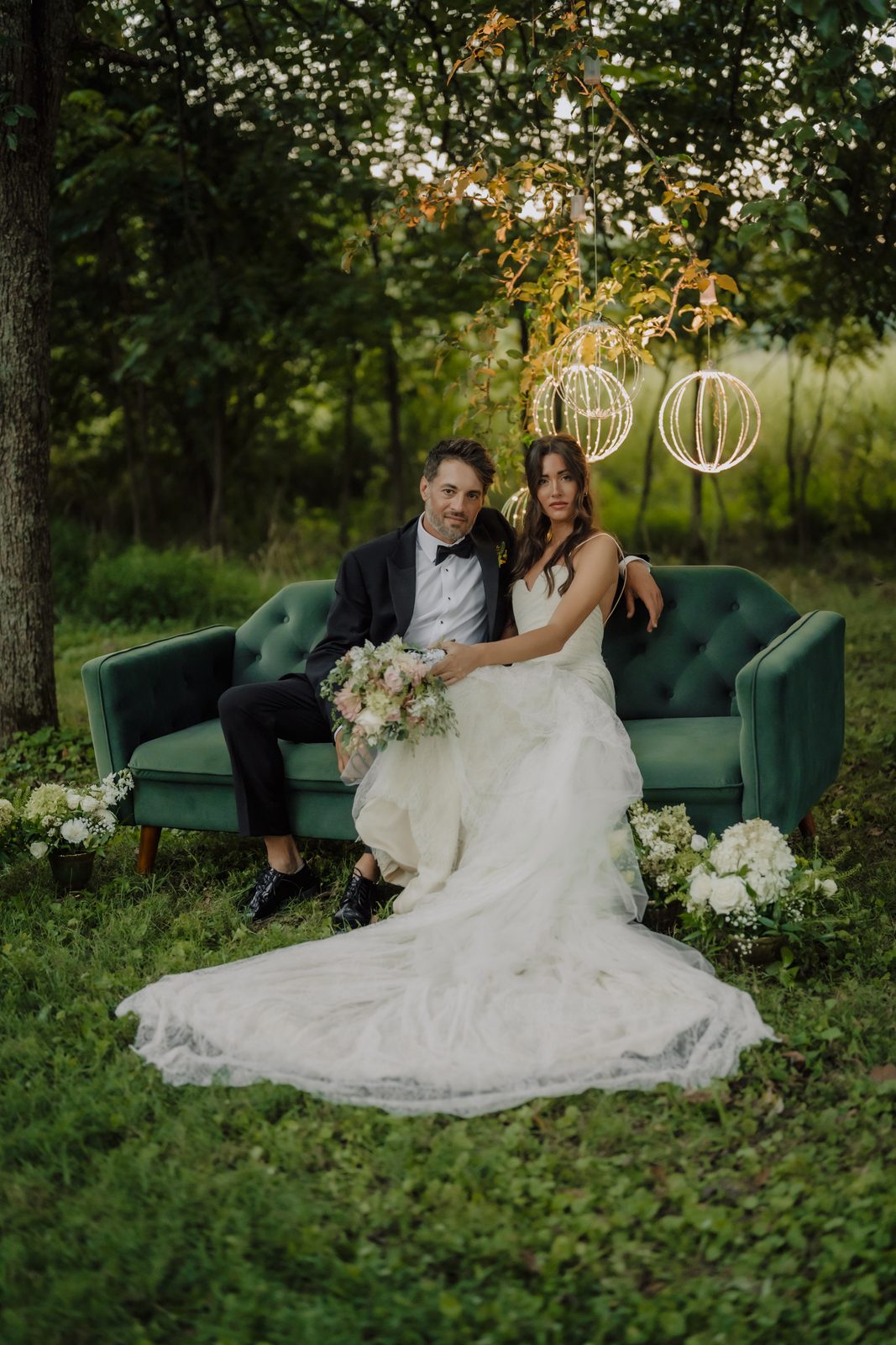 A couple on a green velvet sofa beneath the hanging lights at Drakewood Farm
